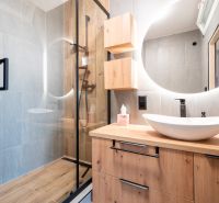 A bathroom with a shower, a sink on a wooden decor, and a round mirror.