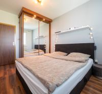 Bedroom in a 2-room apartment with a double bed, mirrored wardrobe, and wooden decor flooring.