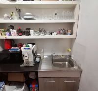 A kitchen in a commercial space with a sink, coffee maker, and shelves with dishes.