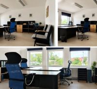 Office space with desks, chairs, and shelves, with large windows and a bright interior.