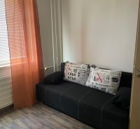 A sofa with colorful cushions, orange curtains, a floor with a wooden decor, a 3-room apartment.