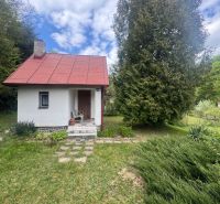 A cottage in Svinica surrounded by greenery, with a white facade and a red roof.