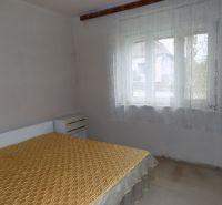 A bedroom in a family house with simple furnishings and curtains on the window.