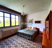 Bedroom in a family house with large windows, carpet, and a bed with pillows.