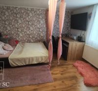 A bedroom in a family house with floral wallpaper, a bed, and a wooden decor floor.