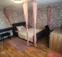 A bedroom in a family house with floral wallpaper, a bed, and a wooden decor floor.