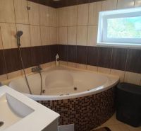 A bathroom in a family house with a corner bathtub and tiles in a wood decor.