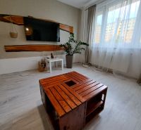 Living room in a 3-room apartment with a television, wooden table, and white curtains.