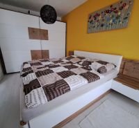 A bedroom in a three-room apartment with a bed, a large wardrobe, and a yellow wall.