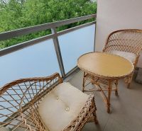 A balcony of a 3-room apartment with chairs and a table, green trees in the background.