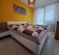 A bedroom in a 3-room apartment with white curtains and a yellow wall, and a floor with a wooden decor.