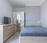 A bedroom with a wood-patterned floor, a wardrobe, a dresser, and a television.