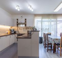 A kitchen with white cabinets, a dining table, a wooden decor floor, bright windows.