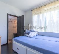 A room in a family house with a bed, a dresser, and large windows.
