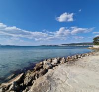 The coast in Sukošan with clear water and a rocky shore under a blue sky.