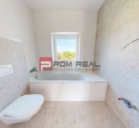 A bathroom in a family house with a bathtub, a window, and light-colored tiles on the walls and floor.