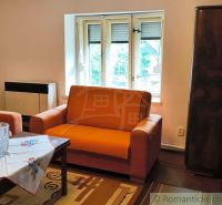 A cottage with an orange sofa set, wooden decor, and an embroidered tablecloth.