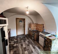 A kitchen in a cottage with a tiled stove and a floor with a wooden decor.