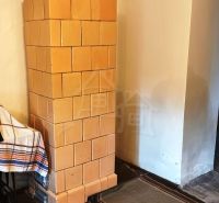 Tiled stove in the interior of a cabin with a wooden decor floor and woven rugs.