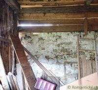 Interior of a cottage with a stone wall and wooden beams, suitable for renovation.