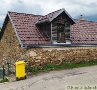 A stone cottage in Hermanovce with a metal roof and a yellow waste container.