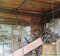A wooden interior of a cabin with decaying boards and a stack of wood.