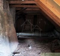 The attic in a wooden cabin with a beamed ceiling and a stone wall.