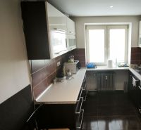A kitchen with dark furniture, a white countertop, and a tiled floor in a 3-room apartment.
