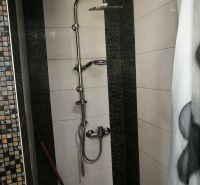 A shower corner in a 3-room apartment with black and white tiles and a shower curtain rod.
