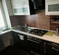 A kitchen in a 3-room apartment with a stove and a sink, surrounded by dark brown tiles.