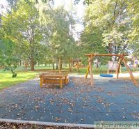 A playground with a slide and swings in the gardens of Hruboňovo, surrounded by greenery.