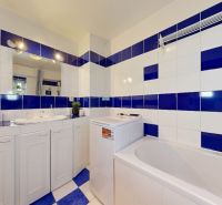 A bathroom in a studio apartment with white and blue tiles, a bathtub, and a washing machine.