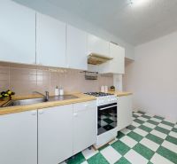 Kitchen in a one-room apartment with white cabinets and green and white tiles.