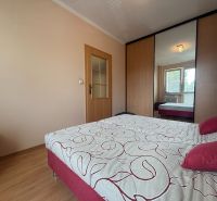 A bedroom with white walls, a wooden decor floor, a wardrobe, and a large bed.