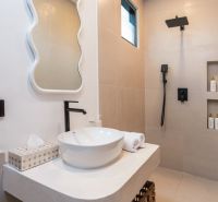 Bathroom in the villa with a countertop sink, mirror, and shower with black accessories.