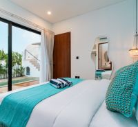 A bedroom in a villa with a pool, turquoise accessories, and large glass doors.