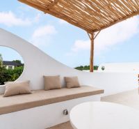 A terrace in a villa in Bali with white walls, an umbrella, and a wooden ceiling.