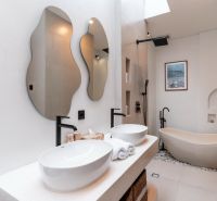 A modern villa bathroom with a marble bathtub, sinks, and mirrors of irregular shapes.