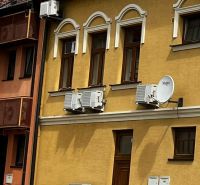 Yellow historical building in Topoľčany with air conditioning units and a satellite dish.