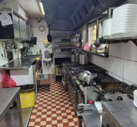 A kitchen in commercial premises with stainless steel counters, stoves, and shelves with dishes.