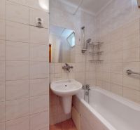 A bathroom with a bathtub and a sink in a three-room apartment, tiled with light tiles.