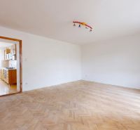 A spacious room with a wooden decor floor leads to a kitchen equipped with appliances.