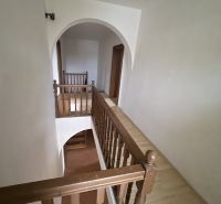 A hallway with an arch and wooden railing in a family house with a wood-patterned floor.