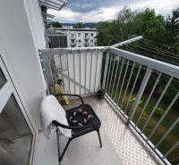 A balcony with a view of greenery and apartment buildings on Nábrežná Street in Trenčín.