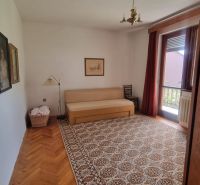 A room in a family house with a sofa, carpet, wood-patterned floor, paintings on the walls.