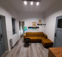 Living room in a family house with a mustard sofa and a wooden-patterned floor.