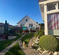 A family house in Orechová Potôň with a well-maintained garden, a walkway, and a dog running around on the lawn.