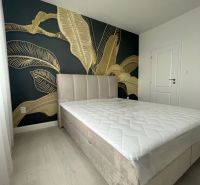 A bedroom in a three-room apartment with a large bed and a bold plant-patterned wallpaper.