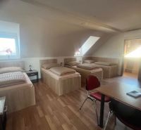 A room with three beds, a wooden floor design, and red chairs by the table.