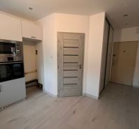 A kitchen in a one-room apartment with a wood-patterned floor and built-in appliances.